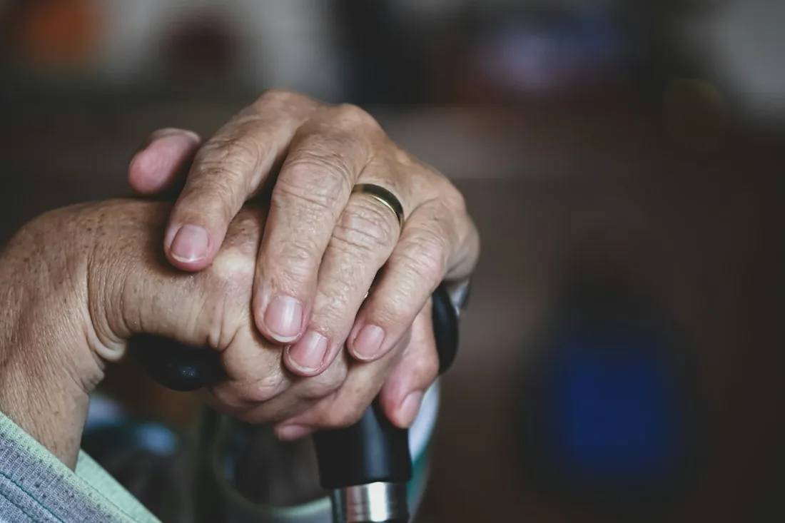 An older person's hands resting on the handle of a walking cane