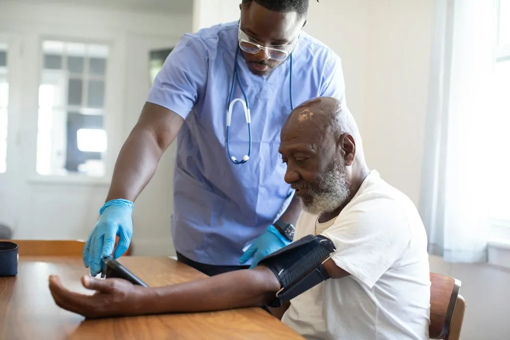 A home care aide checking an older man's blood pressure at his kitchen table
