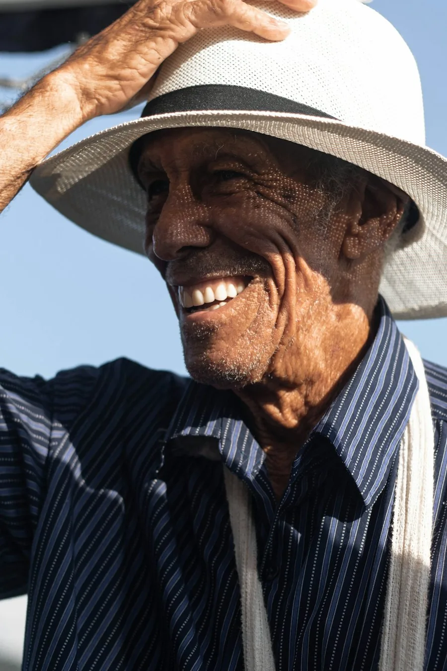 An older man in a panama hat smiling in the sunshine