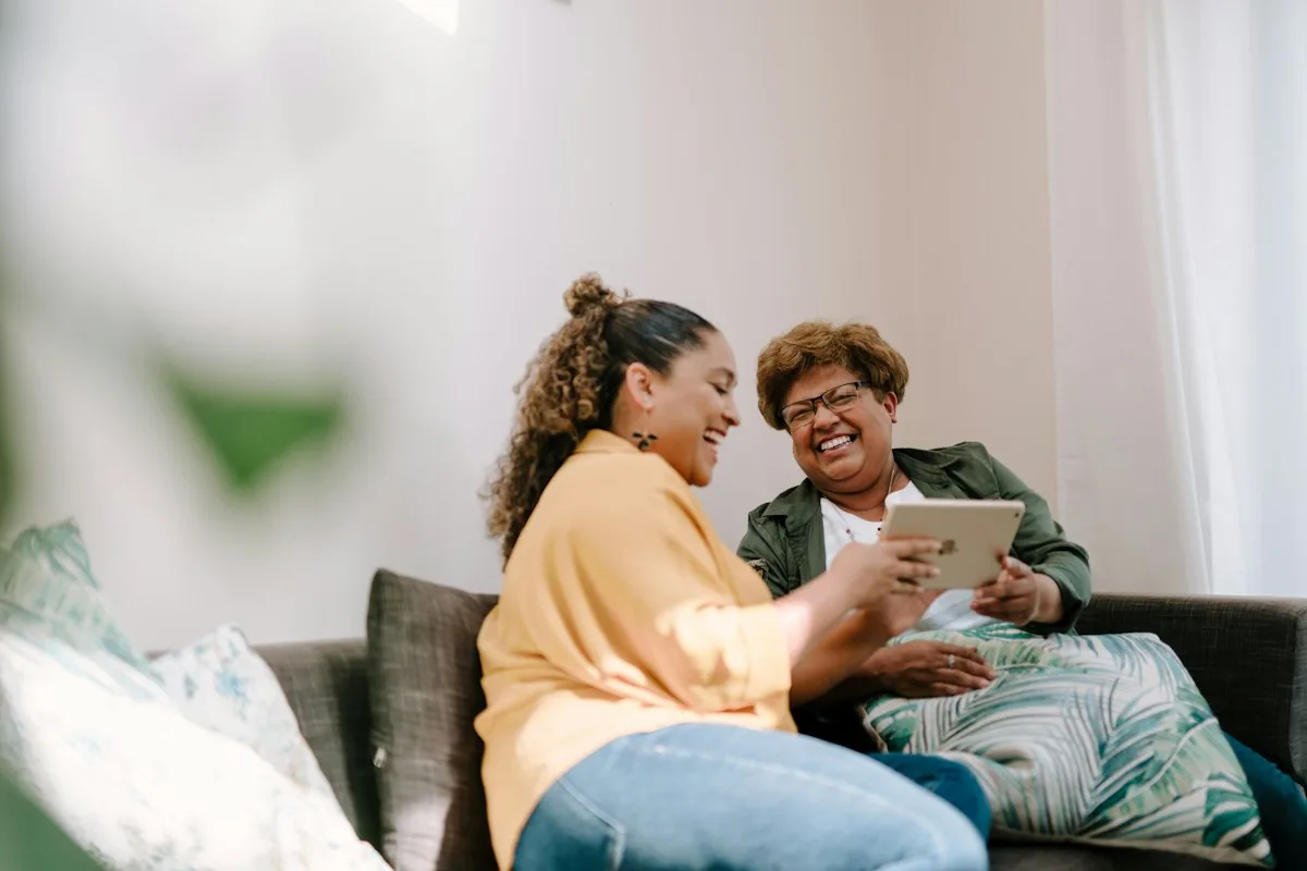 A daughter and her mother laughing together over a tablet