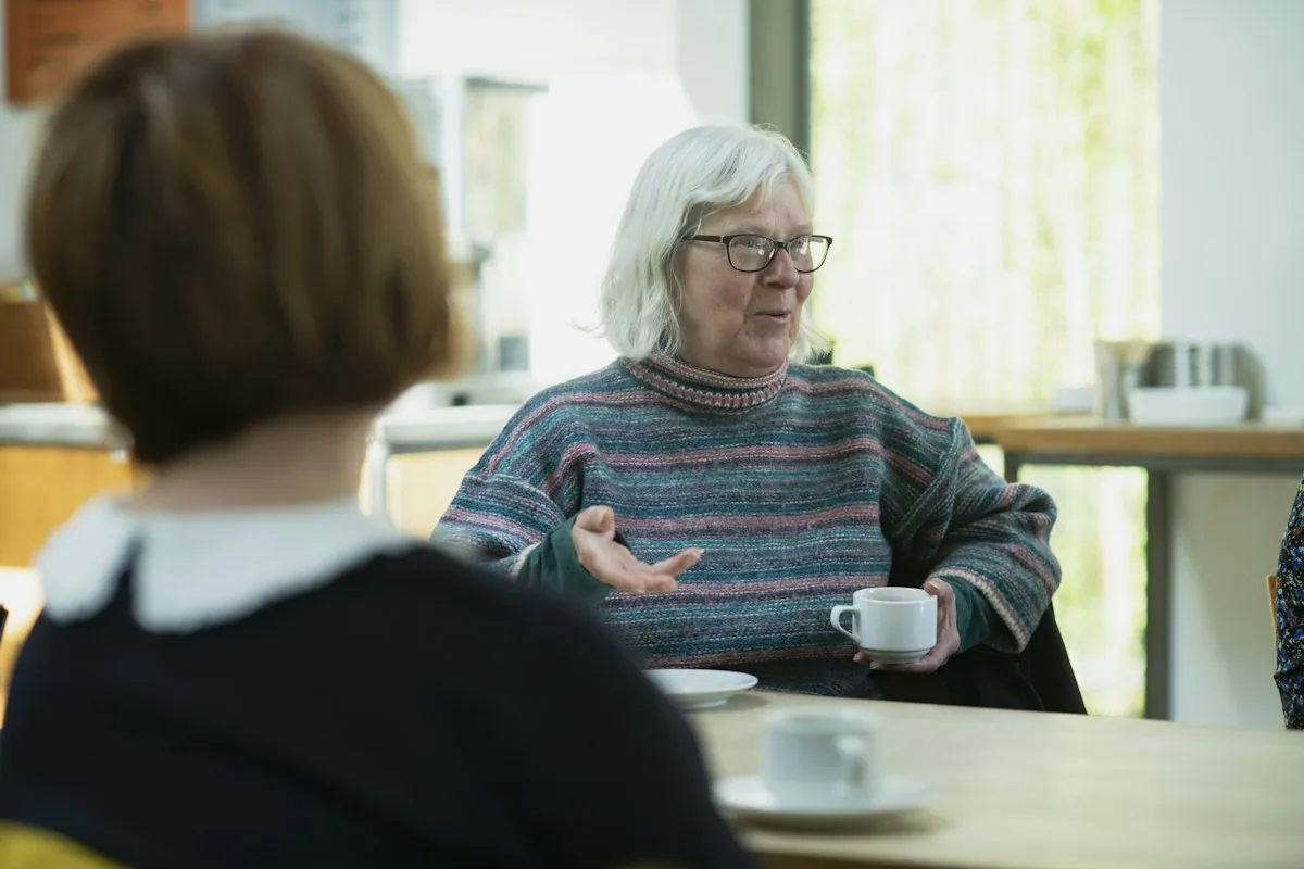 Two people talking across a table over cups of coffee
